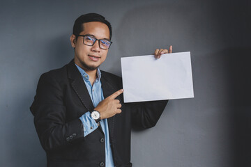 Asian businessman pointing empty white sheet, on grey background. Place for your advertising and text. Template for your Advertisement. Man Holding Empty Banner, free space
