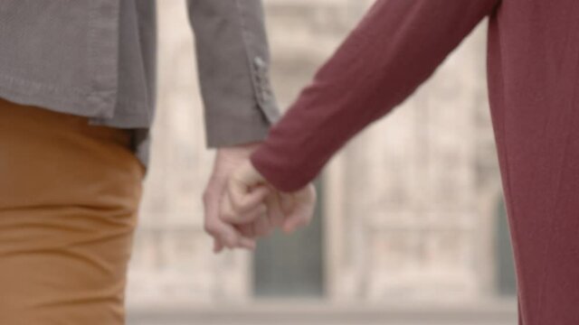 two boyfriends, a boy and a girl, shake hands and walk together in a square of a city