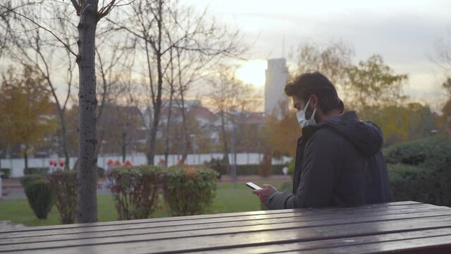 Man On The Go Wearing Covid19 Mask. Man looking at the phone. Park sunset.