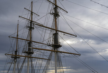 Masts of a large sailing ship with a cloud covered sky background.