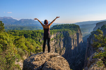 A girl with her arms raised high is standing on the edge of a deep canyon. Turkey
