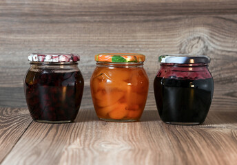 There are three jars of homemade jam on the wooden table. Image with selective focus.