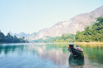 Fototapeta na wymiar Dtraditional wooden boat with water, sky and mountains in Ratchaprapha Dam or Khao sok national park, Thailand