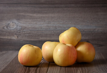 There are several yellow apples on the wooden table. Image with selective focus.