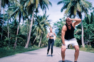 Obraz premium Sport lifestyle. Jogging outdoors. Young couple running under palm trees. Man is tired because of heat.