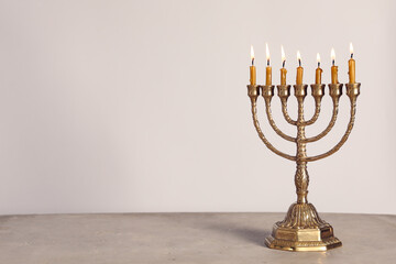 Fototapeta premium Golden menorah with burning candles on table against light grey background, space for text