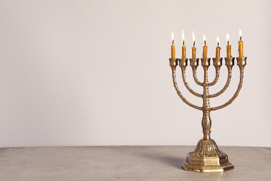 Golden menorah with burning candles on table against light grey background, space for text