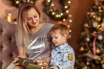 Fototapeta na wymiar Smiling young girl and boy sit in a decorated Christmas room and enjoy the holiday and gifts.