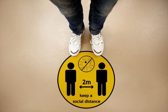 Keep social distance as preventive measure during coronavirus outbreak. Yellow warning sign on floor in front of man, top view