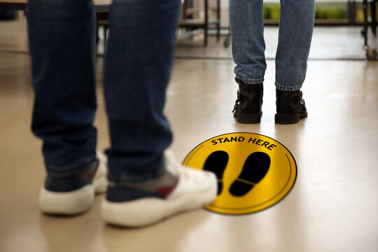 Keep social distance as preventive measure during coronavirus outbreak. Yellow warning sign on floor between people, closeup