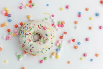 Rolgordijnen Heerlijke donut met suikerglazuur en kleurrijke decoratie. Versierd met veelkleurige snoep op witte achtergrond. Horizontaal beeld. Bovenaanzicht. © Albert Ziganshin