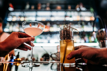 the hands of customers customers hold their cocktails on the background of the styling with alcohol in the bera on the bar counter