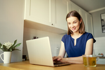 Working at home. Freelance concept. Pretty young woman using laptop in kitchen.