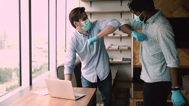 African employee greet colleague make elbow bump gesture, staff wear surgical face masks and protective gloves work together using laptop in modern office. Personal safety, stop covid spread concept
