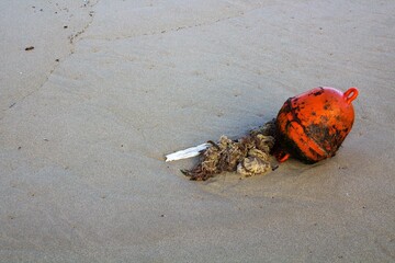 evocative closeup image of abandoned buoy on sandy beach with rough seas and small island in the background