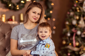 Obraz na płótnie Canvas Smiling young girl and boy sit in a decorated Christmas room and enjoy the holiday and gifts.
