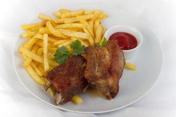 Fried pork ribs with French fries and ketchup on a white plate