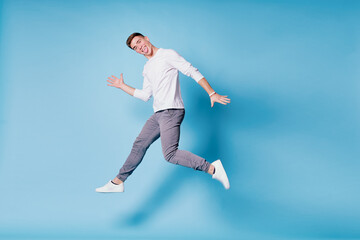 Naklejka na ściany i meble Colorful studio portrait of happy young man dancing jumping against blue background.