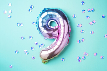 Creative layout. Rainbow foil balloon number and digit nine 9. Birthday greeting card. Anniversary concept. Top view. Copy space. Stylish colored numeral over blue background. Numerical digit.