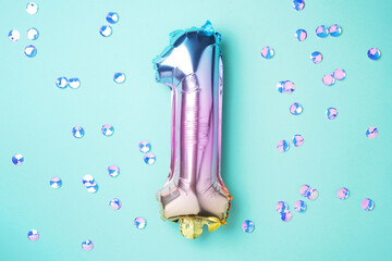 Creative layout. Rainbow foil balloon number and digit one 1. Birthday greeting card. Anniversary concept. Top view. Copy space. Stylish colored numeral over blue background. Numerical digit.