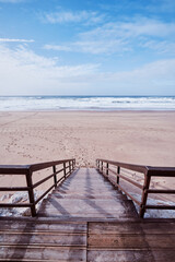 Fototapeta na wymiar Wooden stairs heading down to the oceanbeach as sea foam and waves roll in. Portugal.