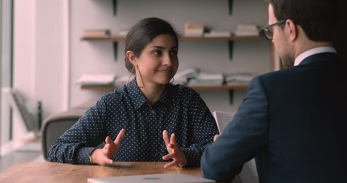 Young Indian female applicant pass job interview for enterprise company position, job seeker introduce herself answers questions talk to man company hr manager. Business negotiations in office concept