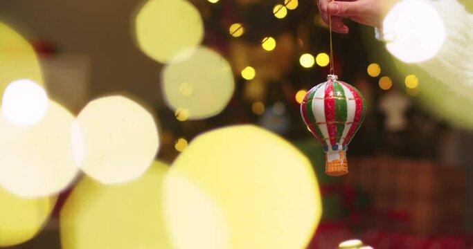 Close up of woman's hand holding Christmas tree toy in the form of parachute in light of Christmas lights. Concept of family holidays, perfect Christmas, New Year, celebration.