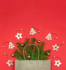Poster Kerstcompositie, kopieer ruimte. Papieren zak met kerstboomtakken en houten speelgoed op rode achtergrond. Kerst komst en cadeau levering concept. © Albert Ziganshin
