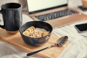 Breakfast in bed: a wooden tray with granola and cup of cocoa with a laptop on background.