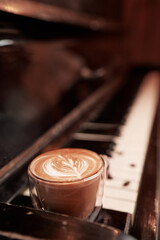 Aroma music. Cup of cappuccino coffe on the piano keyboard.