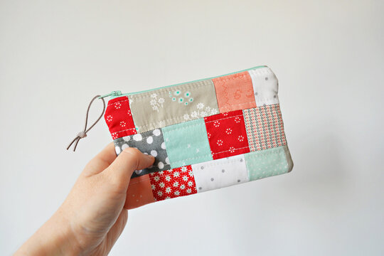 Hand holding colorful patchwork quilted zipper pouch over white