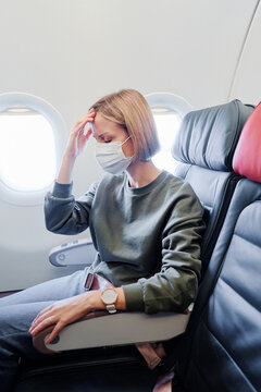 COVID-19 Young woman with KN95 FFP2 mask feeling unwell on plane. Fear of flying woman in airplane. Stress, headache, motion sickness and airsickness on plane during pandemic.