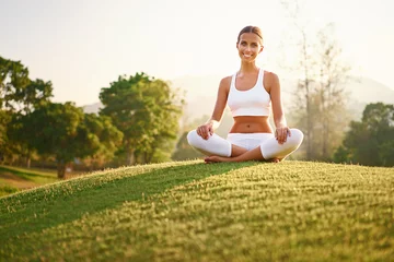  Yoga at park with view of the mountains, with sunlight. Young woman in lotus pose sitting on green grass. Concept of calm and meditation. © luengo_ua