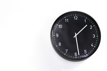 a big round black clock is installed at the white cement wall in the bedroom of the house