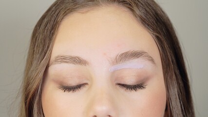Female face with closed eyes. Close-up. Hot wax on the eyebrows to remove excess hair. Wax correction of the shape of the eyebrows. Beauty industry close up.