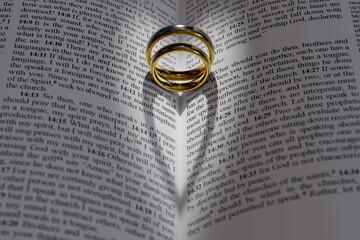 Two wedding rings on a bible, open to Corinthians Chapter 13, 