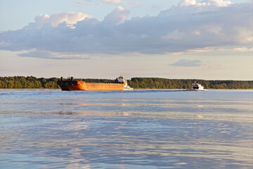 Russian pusher cargo tug ship carries a empty barge on the Volga river on green forest shore, boat and cloudy sky background, side view at summer day, river logistics transportation delivery by water 
