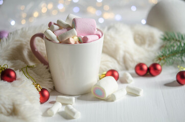 Cup with marshmallows and red balls on a white table.