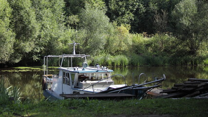 Obraz premium Small old abandoned motor boat on green shore background at Sunny summer day in forest marina