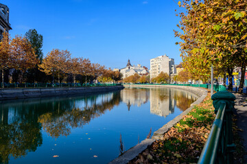 Fototapeta na wymiar Landscape with Dambovita river, old buildings and yellow, orange and brown leaves in large trees in the center of Bucharest, Romania, in a sunny autumn day.