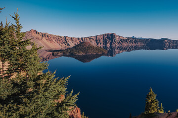 Pine trees, Deep blue lake reflections and Wizard Island at Crater Lake National Park, Oregon, USA. 
