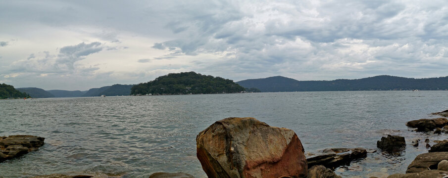 Beautiful panoramic view of a river on a cloudy day with tall mountains and trees in the background, Hawkesbury river, Brooklyn, New South Wales, Australia
