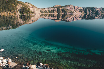 Reflections of Cleetwood Cove on Crater Lake at Crater Lake National Park, Oregon, USA. Crystal clear blue water with visible rocks. 