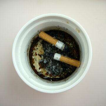 two cigarette butts and ashes in a white cup full of water. World No Tobacco Day