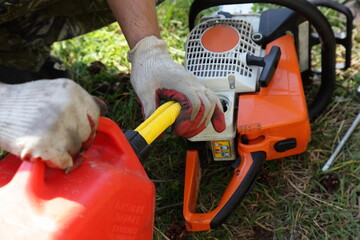 Chainsaw fueling process, filling motorsaw from hand with red can with gasoline fiel mix close up,...