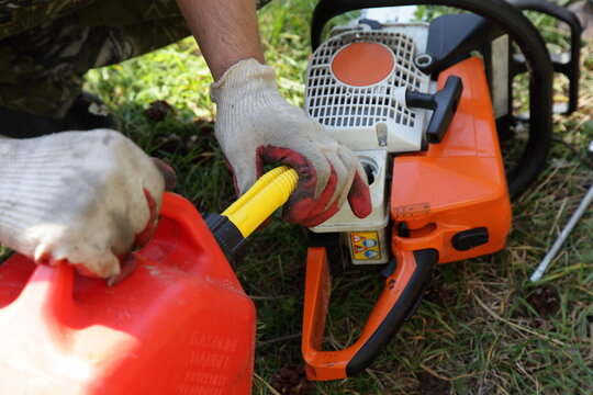 Chainsaw fueling process, filling motorsaw from hand with red can with gasoline fiel mix close up, wood sawing preparation at Sunny summer day on green grass background - Powered by Adobe