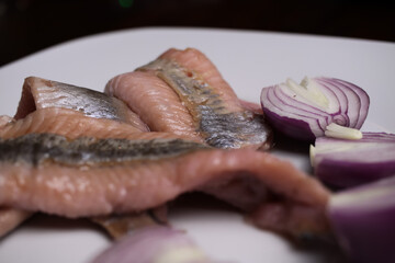 Macro close up of isolated raw salted young herring fish on white plate with onions with high content of omega-3 fatty acids