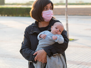 A mother in a surgical mask on the street is holding her baby