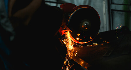 Bright sparks near grinding machine and locksmith sharpening metal part in workshop 