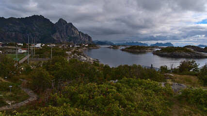 Beautiful view of the rugged mountains on the coast of Austvågøya island, Lofoten, Norway with fishing village Henningsvær, soccer field, houses and rocky islands on cloudy summer day.